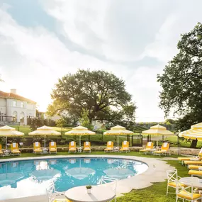 Outdoor pool surrounded by lounge chairs and large oak trees.
