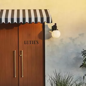 Wooden entrance door beneath black-and-white striped awning labeled “LUTIE’S.”