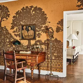Study desk with muraled wall, wooden table, and doorway leading to a bedroom.