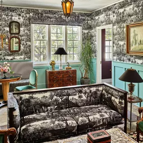 Living room with patterned sofa, green armchair, and wallpaper featuring trees.