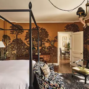 Bedroom with four post bed, patterned rug, and small sitting area.