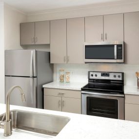 Open-concept kitchen with stainless steel appliances, white quartz countertops and subway tile backsplash, greige cabinetry, and brushed nickel fixtures