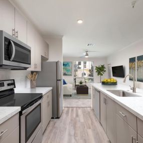 Open-concept kitchen with stainless steel appliances, white quartz countertops and gray subway tile backsplash, greige cabinets with brushed nickel hardware, and wood-like flooring