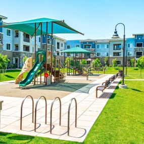 Two playgrounds with slides and benches surrounded by grass and trees