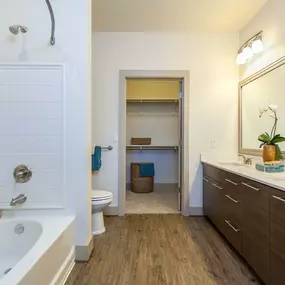 Ensuite bathroom with bathtub and curved shower wall and wood style flooring and double sink vanity adjacent to closet