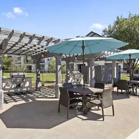 Poolside grilling cabana and seating with light blue umbrellas at Camden Cedar Hills apartments in Austin, TX