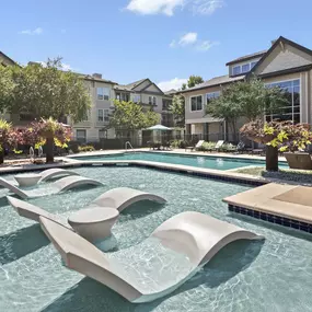 Resort-style pool with in-water loungers and light blue umbrellas at Camden Cedar Hills apartments in Austin, TX