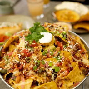 Nachos with charro beans, queso fundido, chile rojo, pico de gallo, pickled onion, green olive, crema