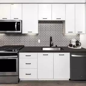 Open-concept kitchen with stainless steel appliances, gray quartz countertops, and timeless ceramic backsplash