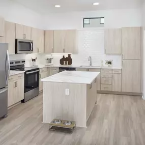 Townhome kitchen with white marbled quartz countertops, large island with storage, and light wood cabinets and wood-style flooring at Camden Belmont apartments in Dallas, TX