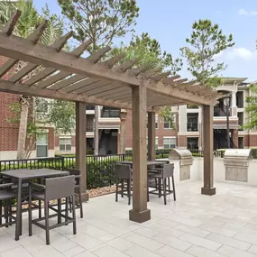 Outdoor grilling area with seating by the pool at Camden Grand Harbor Apartments in Katy, Tx