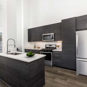 Camden Main and Jamboree Apartments Irvine CA Open concept luxury kitchen with stainless steel appliances, wood-like flooring, chrome pulldown sprayer faucet, dining area, and modern flat cabinets