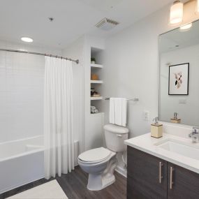 Modern bathroom with white quartz countertops, brushed nickel fixtures, curved shower rod, and extra storage