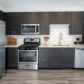 Modern kitchen with stainless steel appliances, white quartz countertops with subway tile backsplash, and wood-like flooring