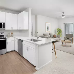 Modern kitchen with stainless steel appliances, white cabinetry, white quartz countertops and open-concept floor plan with sliding glass door to the private patio at Camden Spring Creek Apartments in Spring, Tx