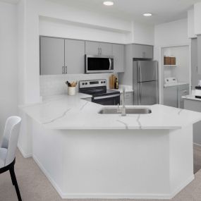 Kitchen with quartz countertops and stainless steel appliances alongside laundry room at Camden Montierra apartments in Scottsdale, AZ