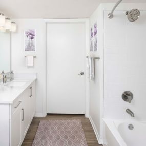 Beautifully renovated bathroom featuring quartz countertops, curved shower rod, rain shower head, satin nickel fixtures and hardware, and LED vanity lighting.