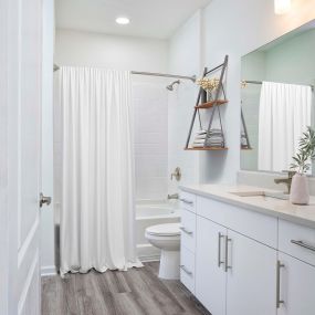 Beautifully renovated bathroom featuring quartz countertops, curved shower rod, rain shower head, satin nickel fixtures and hardware, and LED vanity lighting.