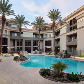 Lighted pool and waterfall with gas grilling stations and dining areas at dusk