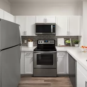 Open-concept kitchen with wood-style flooring, white quartz countertops, white shaker cabinets, gray subway tile backsplash, and stainless steel appliances