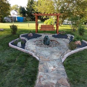 A flagstone walkway leading up to a swinging bench, complimented by various design elements.