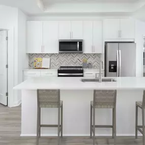 White contemporary apartment kitchen featuring white quartz countertops, herringbone backsplash, and modern white cabinetry at Camden Grandview in Charlotte, NC