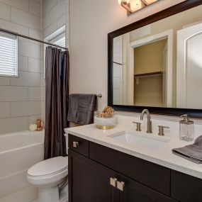The townhomes bathroom with bathtub and shower combination, framed mirror, and under-mount quartz countertop sink