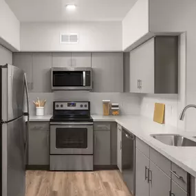 Spacious kitchen with stainless steel appliances, white quartz countertops, white subway tile backsplash, brushed nickel fixtures, and wood-like flooring