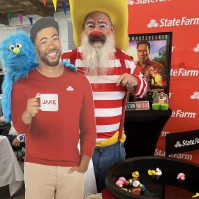 A clown and blue furry puppet standing with Jake cut out at the State Farm booth!