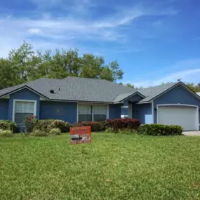 Noland's Roofing recently completed shingle roof project on a blue single-story home in Clermont, FL, with signage indicating a local roofing job.