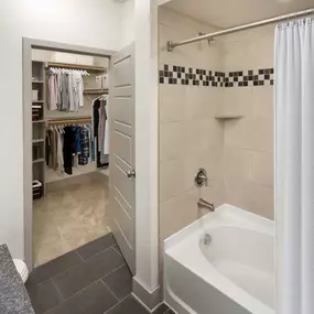 Bathroom with tile flooring bathtub with tile surround and walk in closet with wood shelving