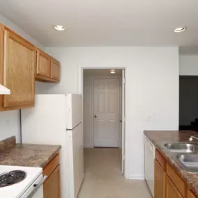 Bright kitchen at The Park at Greenhill featuring wood cabinetry, dual-basin stainless steel sink, white appliances, and laminate countertops, with a clean and functional galley-style layout.