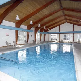 Spacious indoor swimming pool with crystal-clear water at The Park at Greenhill, surrounded by lounge chairs and enclosed by a vaulted wooden ceiling with exposed beams and skylights.