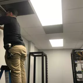 One of The Local Electrician's technicians performing electrical services standing on a ladder in a drop ceiling