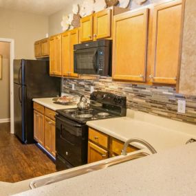 Designer Kitchens with Maple Raised Panel Cabinetry, Black Appliances and Breakfast Bar at Sugarloaf Crossing Apartments