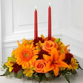 Bright Autumn™ Centerpiece spins the magic of the Fall season with each sun-kissed petal to set your gathering space aglow with blooming beauty. Two taper candles are surrounded by a gorgeous arrangement consisting of orange Asiatic lilies, gerbera daisies and roses with golden Peruvian lilies, burgundy cushion poms and assorted greens to create the perfect addition to your Autumn celebration. GOOD centerpiece is approximately 8