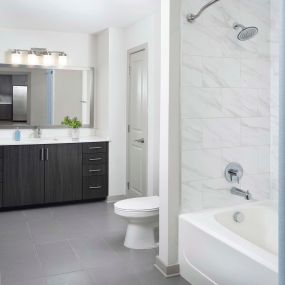 Bathroom with modern tile, marble-like bathtub surround, dark cabinets and light countertops