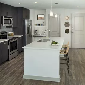 Kitchen with large island, light quartz countertops, brown cabinetry, stainless steel appliances, single-basin sink and built-in bar.