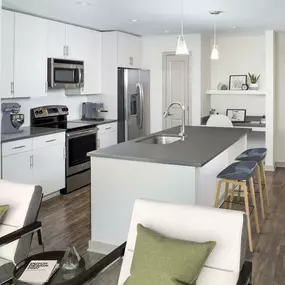 Kitchen with large island, gray countertops, light wood cabinetry, single-basin sink, stainless steel appliances and built-in desk.