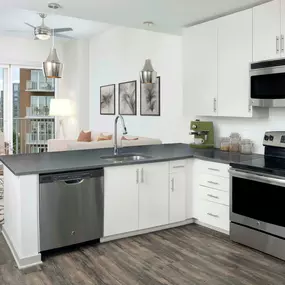 Kitchen with light cabinets, gray countertops, white backsplash, stainless steel appliances, wood-style flooring throughout and private balcony