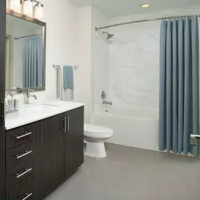 Bathroom with brown cabinetry, light quartz countertops and bathtub with marble-style tile surround.