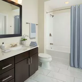 Bathroom with brown cabinetry and tub with tile surround.