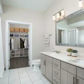 Bathroom with double sinks, light gray cabinetry, bathtub/shower combo and large walk-in closet.