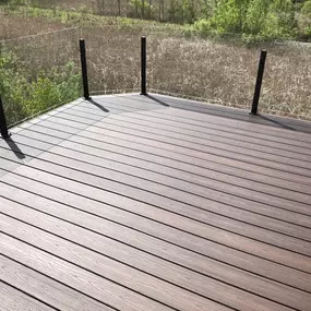 Minimalist composite deck with frameless glass railings overlooking a natural field and greenery