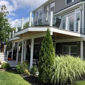 Elevated glass railing deck with white framing and a covered patio beneath, featuring a landscaped garden