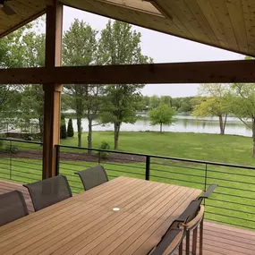 Covered lakefront custom deck with ceiling, metal railings, and a spacious dining area overlooking a serene landscape