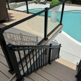 Stylish poolside deck with glass panel railings and black metal framing in Commerce Charter Twp, MI. Built by Cedar Works, this design blends safety, luxury, and durability with direct access to the pool area.