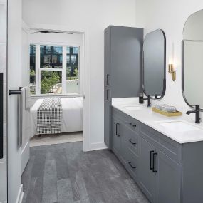 Ensuite bathroom with double vanity, walk-in shower, and wood-style flooring at Camden Durham apartments in Durham, NC.