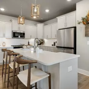 Kitchen with white cabinets and island with 3 barstools at DRB Homes Wadsworth Manor