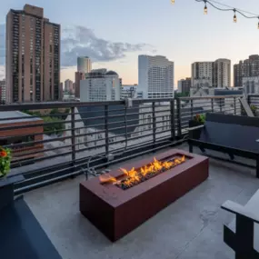 ELEVATE Apartment Homes rooftop deck with a fire pit and a city skyline at dusk